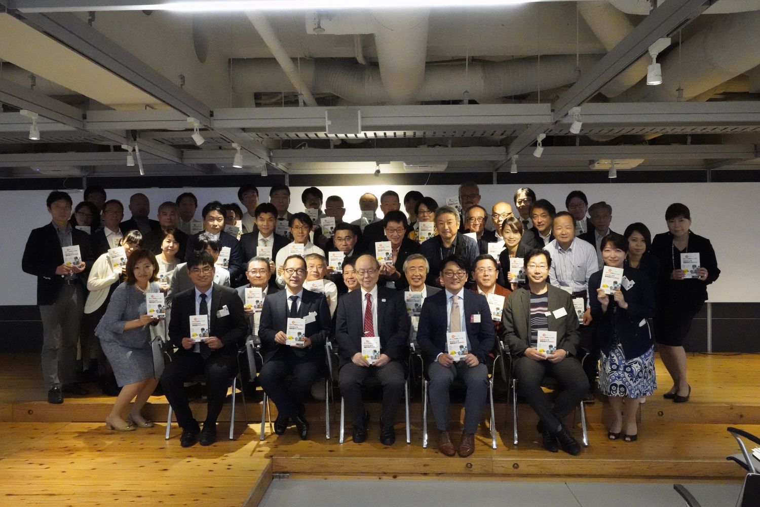 参加者による記念撮影。編著『今選ぶなら、地方小規模私立大学！』を手に